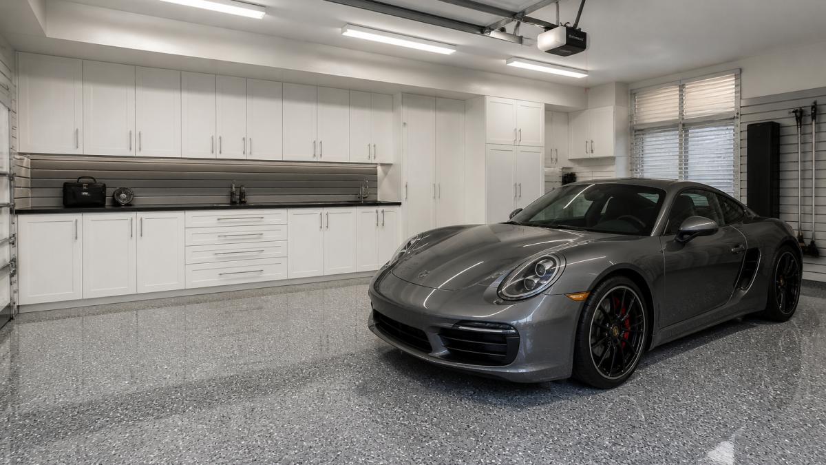 A freshly finished double garage interior with glossy gray epoxy flooring, custom white cabinetry along the back wall, and a luxury sports car parked under bright LED lighting