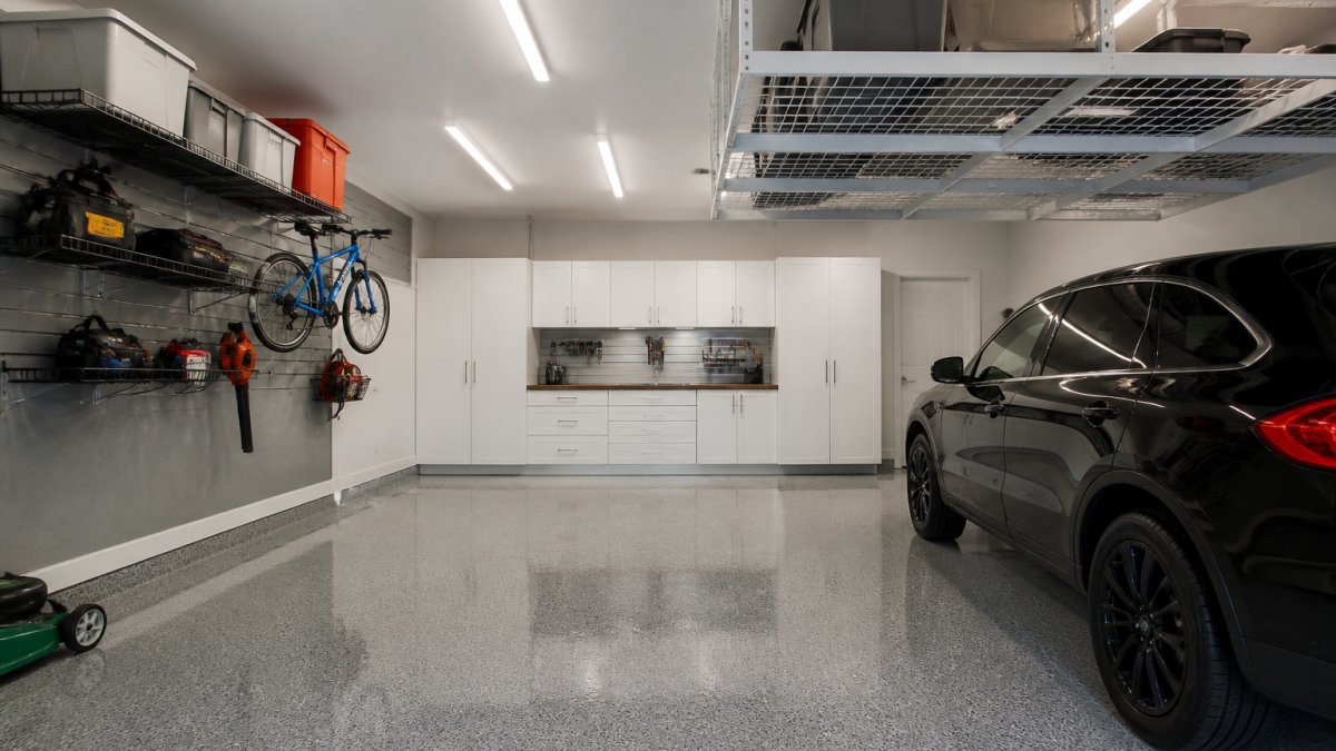 Custom white cabinets and steel shelving in a garage storage system with a glossy epoxy floor.